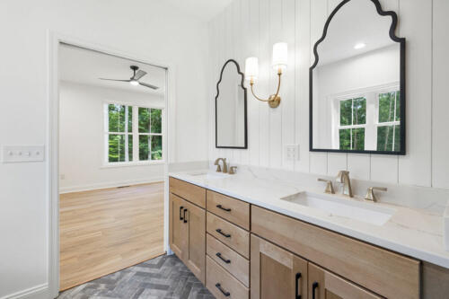 The Corbisiero - elegant full bathroom with natural wood cabinets and double vanity sinks, by Caliber Homebuilder